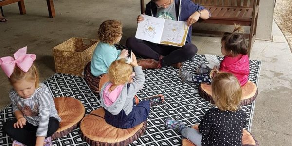 toddlers sat on a mat reading a book with a teacher